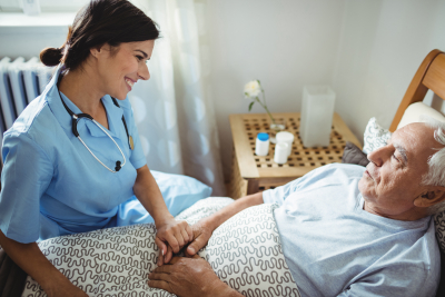 Nurse holding the hands of elder man in bedroom